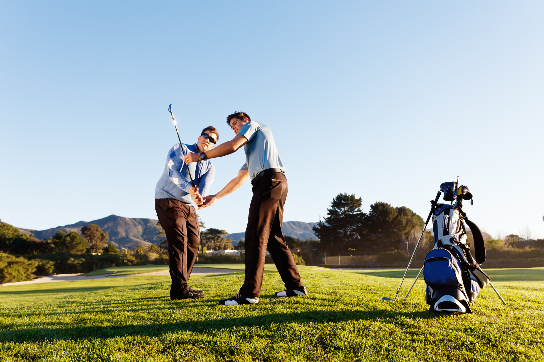 Golf lesson: young coach helping golfer on beautiful golf course